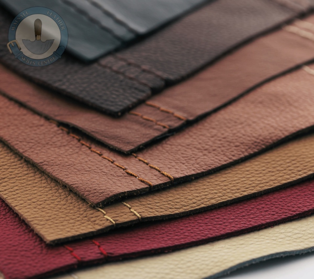 A photo of seven pieces of leather all with two stitching lines running parallel down one side, showing pieces used to practice basic leather skills. The Walsall Leather Skills Centre logo is at the top of image.