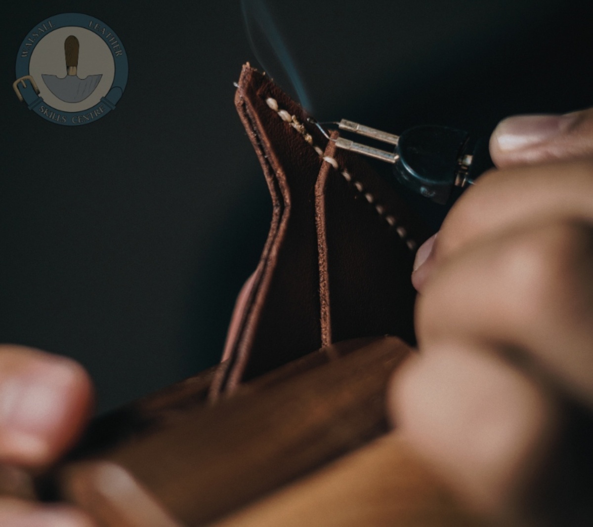 A close-up photo of someone using small precision tools to ensure accuracy with the stitching on patch of leather. The leather is secured in a clam. The Walsall Leather Skills Centre logo is at the top of image.