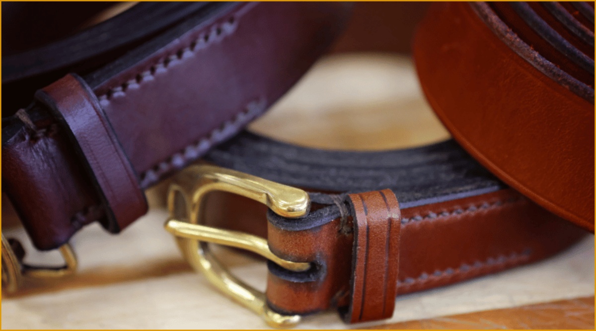 A close up photo of three handmade leather belts with edged keepers, burnished edges and gold metalwork and buckles.