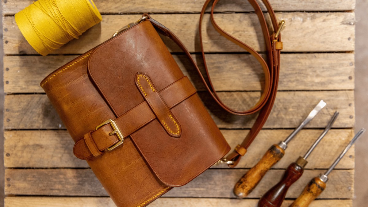 A hand made leather bag made by tutor Jo Heard along with leather work tools and waxed thread.